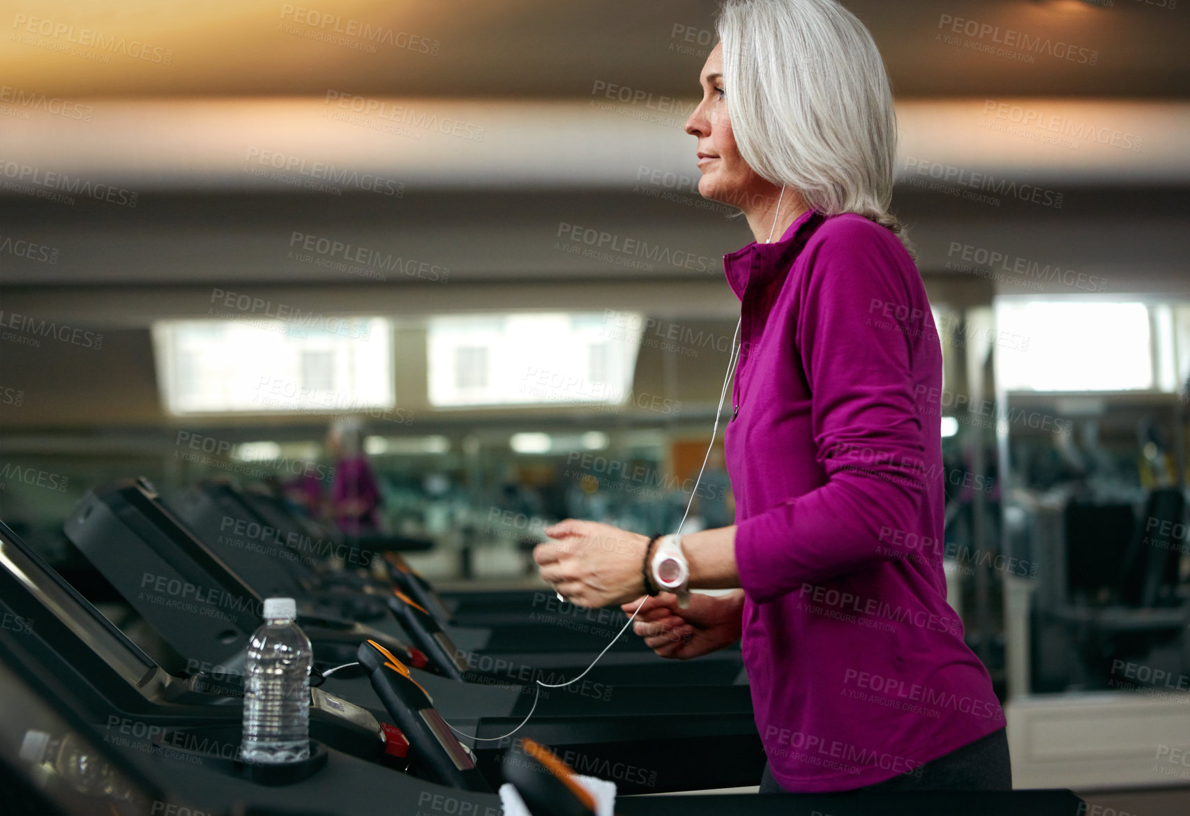 Buy stock photo Senior woman, running on treadmill and training by music in gym club, water and bottle for health in wellness. Mature, female runner and exercise with podcast, hydration and workout by speed machine