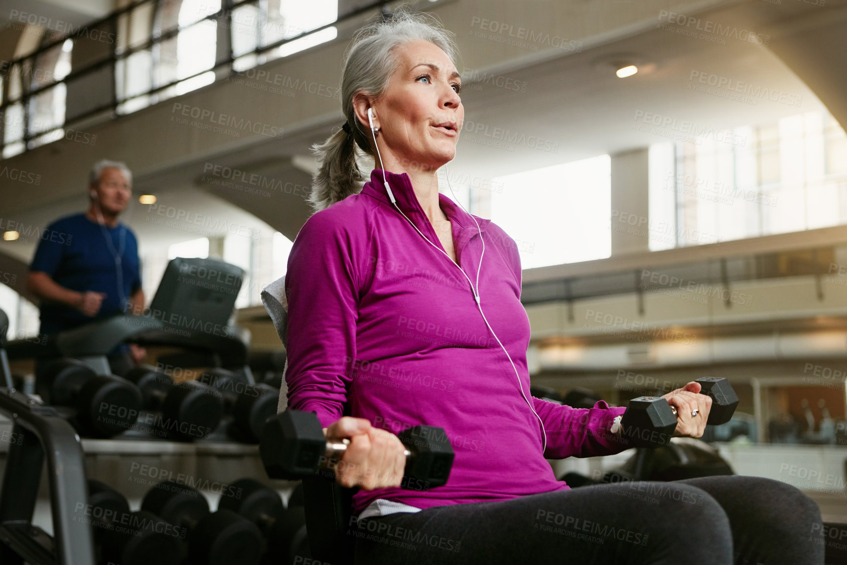 Buy stock photo Fitness, dumbbell and senior woman at a gym for training, wellness and cardio with earphones, music or mindset. Weightlifting, bodybuilding and elderly female person at sports center for arm workout