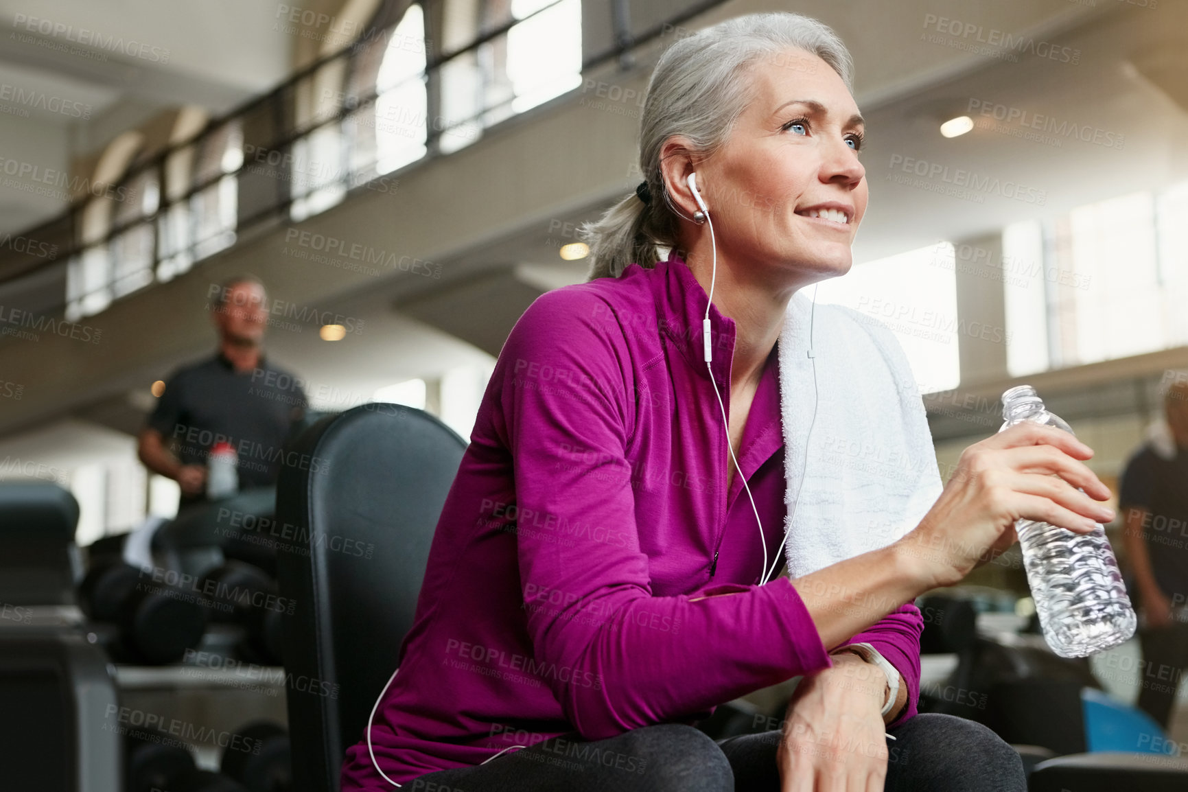 Buy stock photo Mature woman, relax and drinking with water, earphones or thinking for music, workout or exercise at gym. Female person with smile for break, mineral beverage or thirst after training at health club