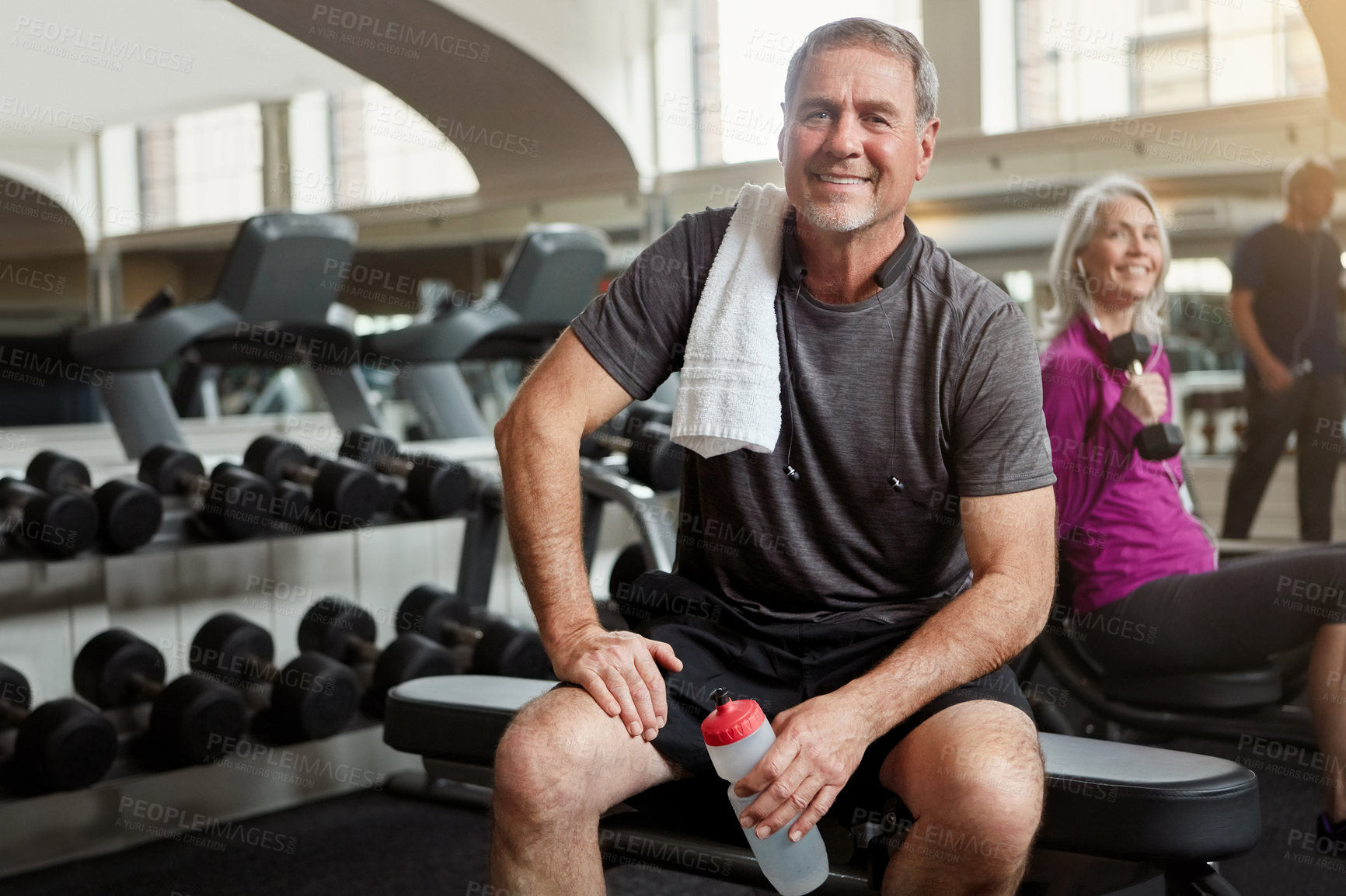 Buy stock photo Shot of a senior group of people working out together at the gym whilst a mature man takes a break