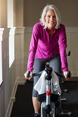 Buy stock photo Shot of a happy senior woman on a stationary bike