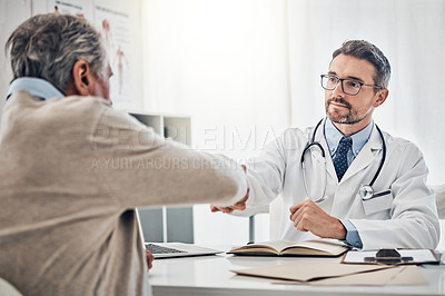 Buy stock photo Shot of a friendly doctor shaking hands with his mature patient over the table