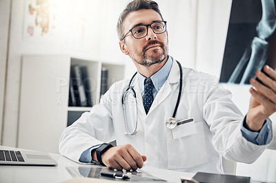 Buy stock photo Shot of a focused doctor looking at an x-ray while sitting at his desk