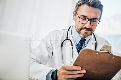 Buy stock photo Shot of a focussed doctor looking at paperwork on a clipboard while sitting at his desk