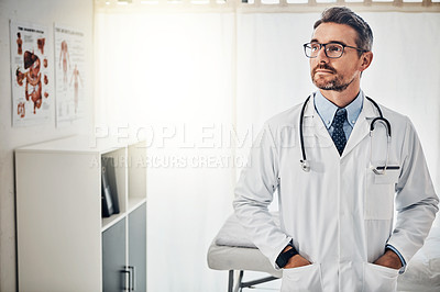 Buy stock photo Shot of a a focussed doctor standing with his hands in his pockets in his consultation room