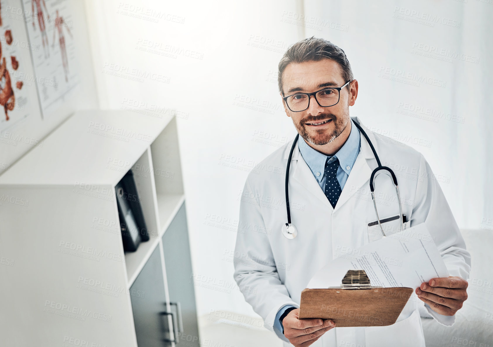 Buy stock photo Portrait of a focussed doctor reading a patient file while standing in his consultation room