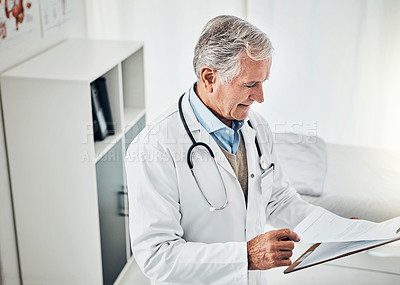 Buy stock photo Shot of a mature doctor reading a patient file while standing in his consultation room