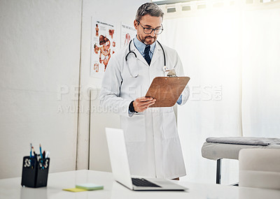 Buy stock photo Shot of a focussed doctor reading a patient file while standing in his consultation room