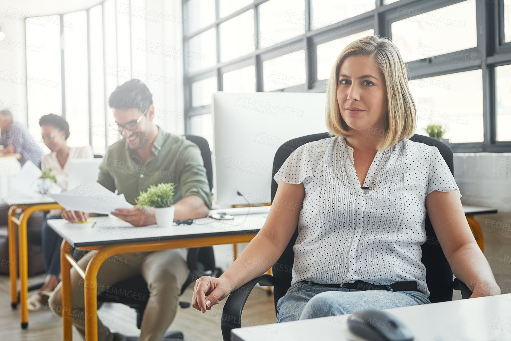 Buy stock photo Shot of a young designer in an office with her colleagues in the background