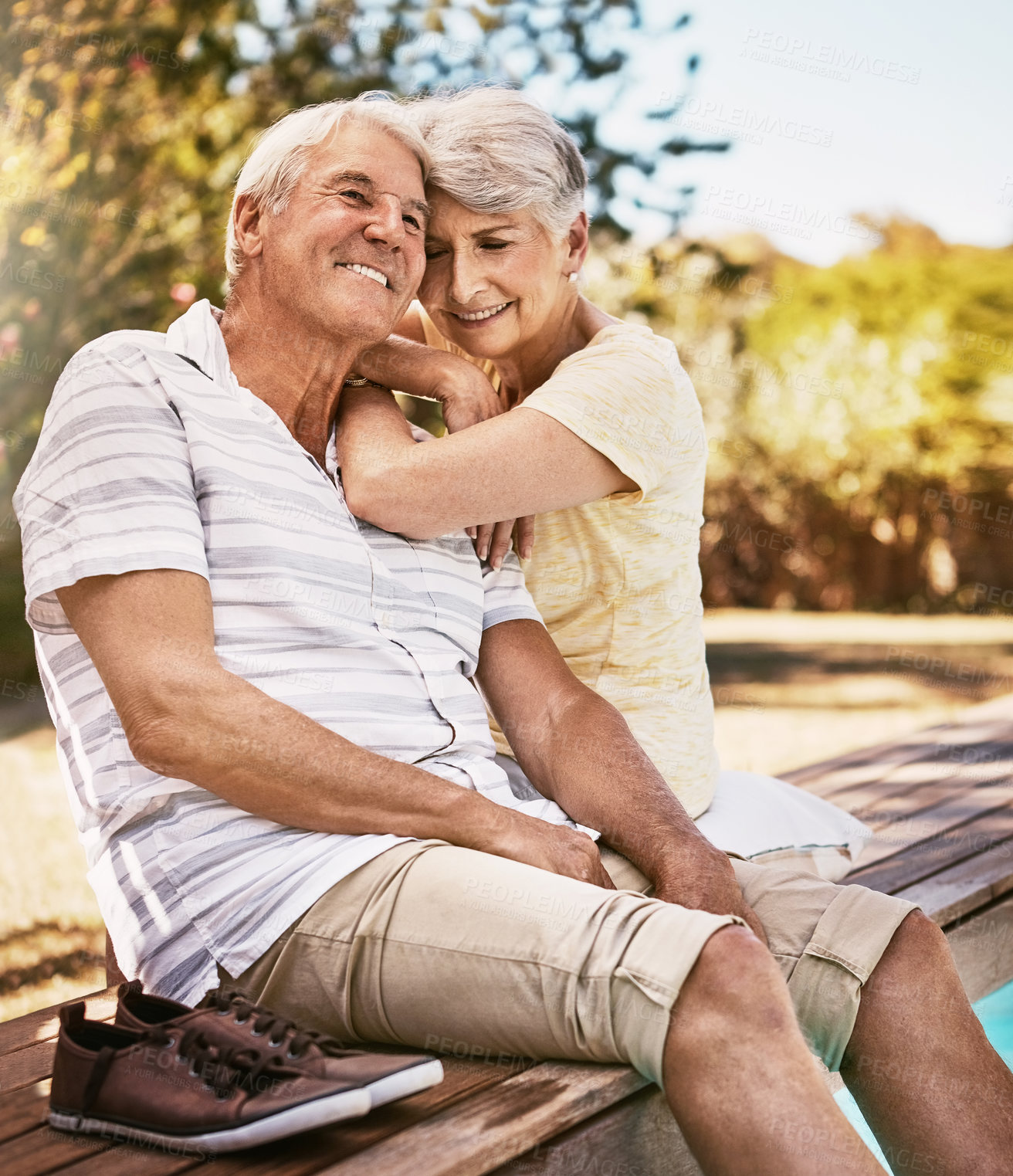 Buy stock photo Senior couple, relax and smile by pool in love and summer vacation, bonding or quality time together in the outdoors. Happy elderly man and woman relaxing and hugging by the water at a poolside