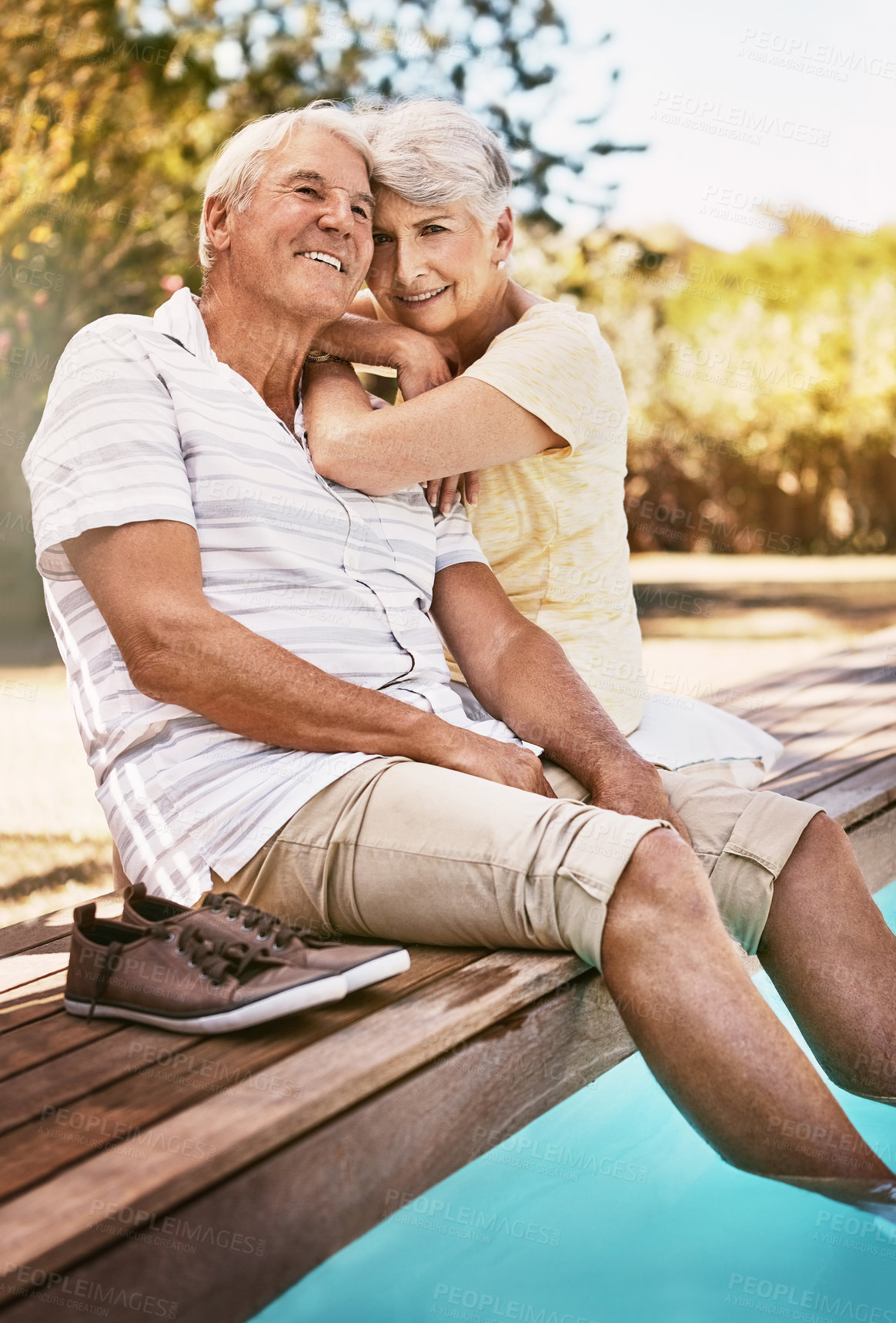 Buy stock photo Senior couple, relax and smile for pool, love and summer vacation, bonding or quality time together in the outdoors. Happy elderly man and woman relaxing and hugging with feet in water by a poolside