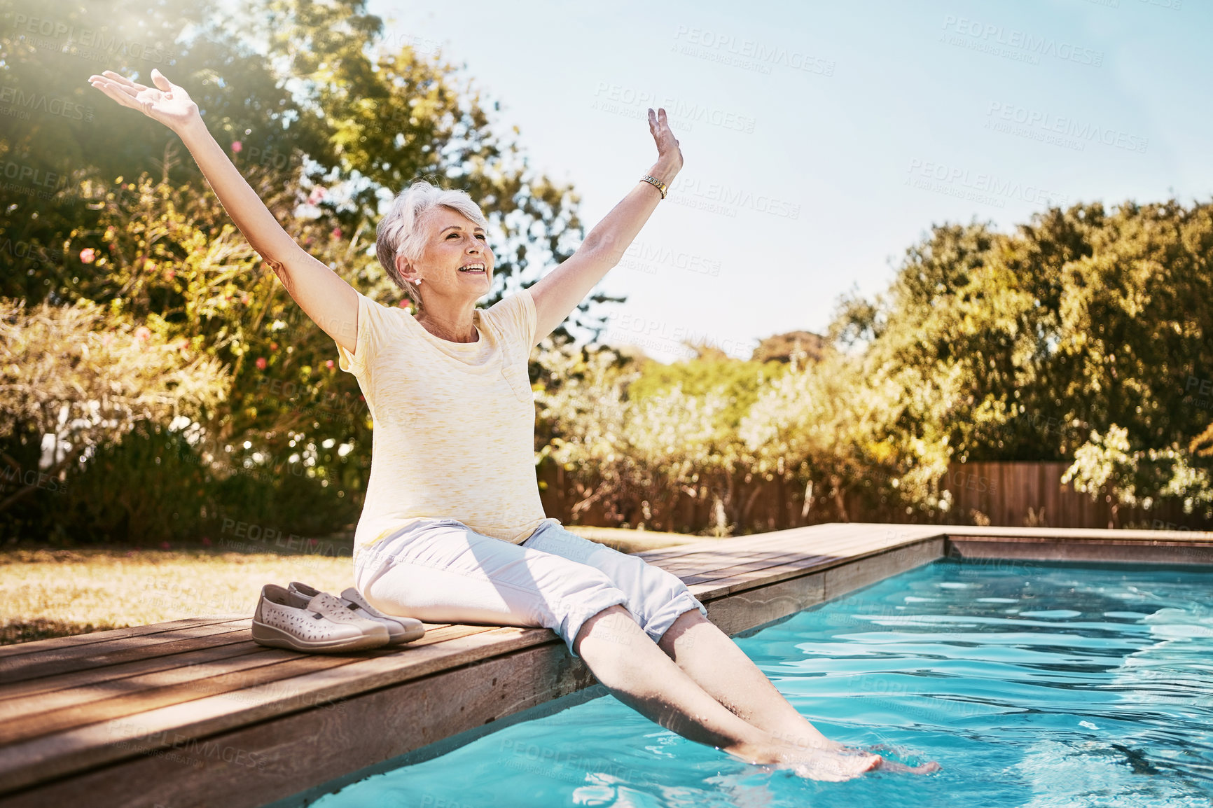 Buy stock photo Shot of a joyful senior woman dipping her feet in a swimming pool with her arms outstretched