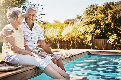 Buy stock photo Senior couple, hug and relax by swimming pool for love or quality bonding time together on summer vacation. Happy elderly man holding woman relaxing with feet in water by the poolside outside
