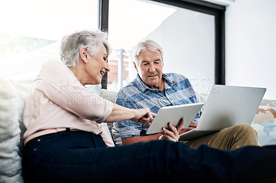 Buy stock photo Shot of a senior woman using digital tablet while her husband uses a laptop at home