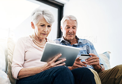 Buy stock photo Shot of a senior couple making a credit card payment on a digital tablet at home