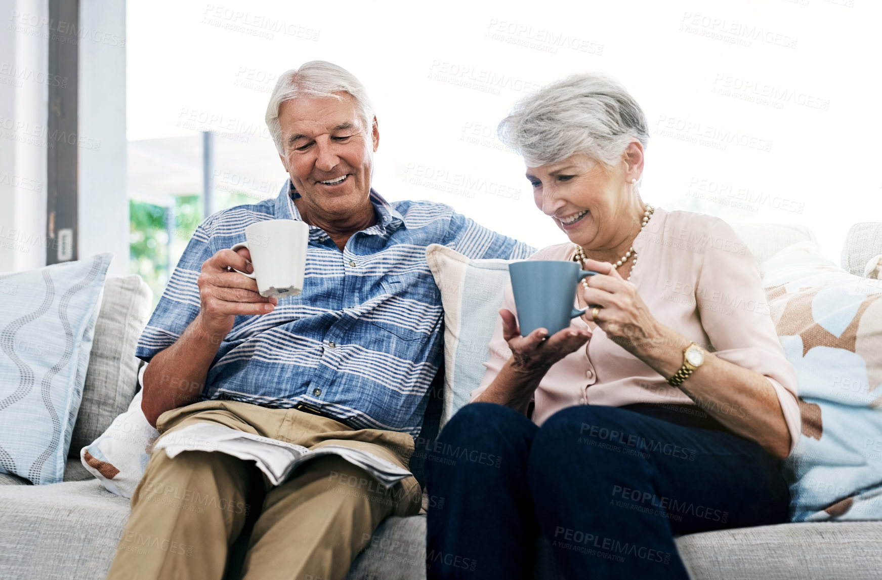 Buy stock photo Shot of a senior couple having coffee and reading a newspaper on the sofa at home