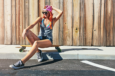 Buy stock photo Shot of a young woman sitting on her skateboard on a sidewalk