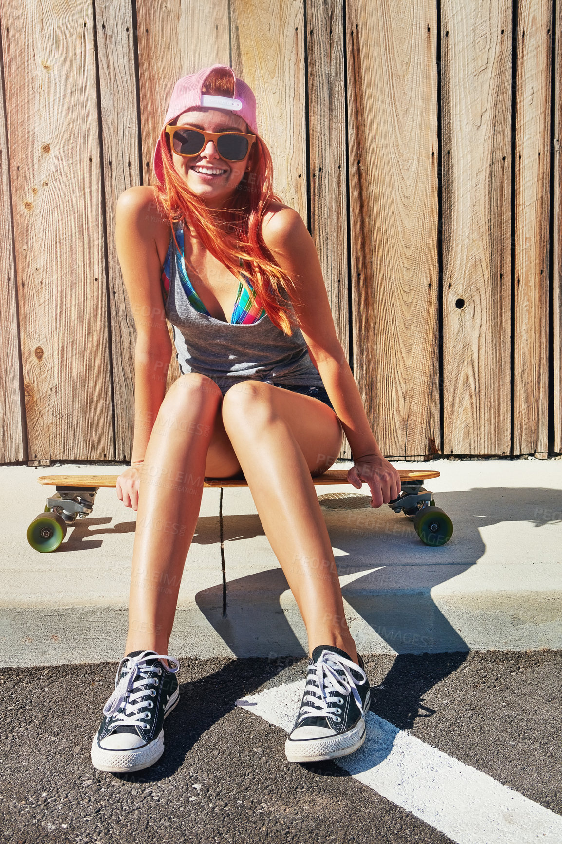 Buy stock photo Shot of a young woman sitting on her skateboard on a sidewalk