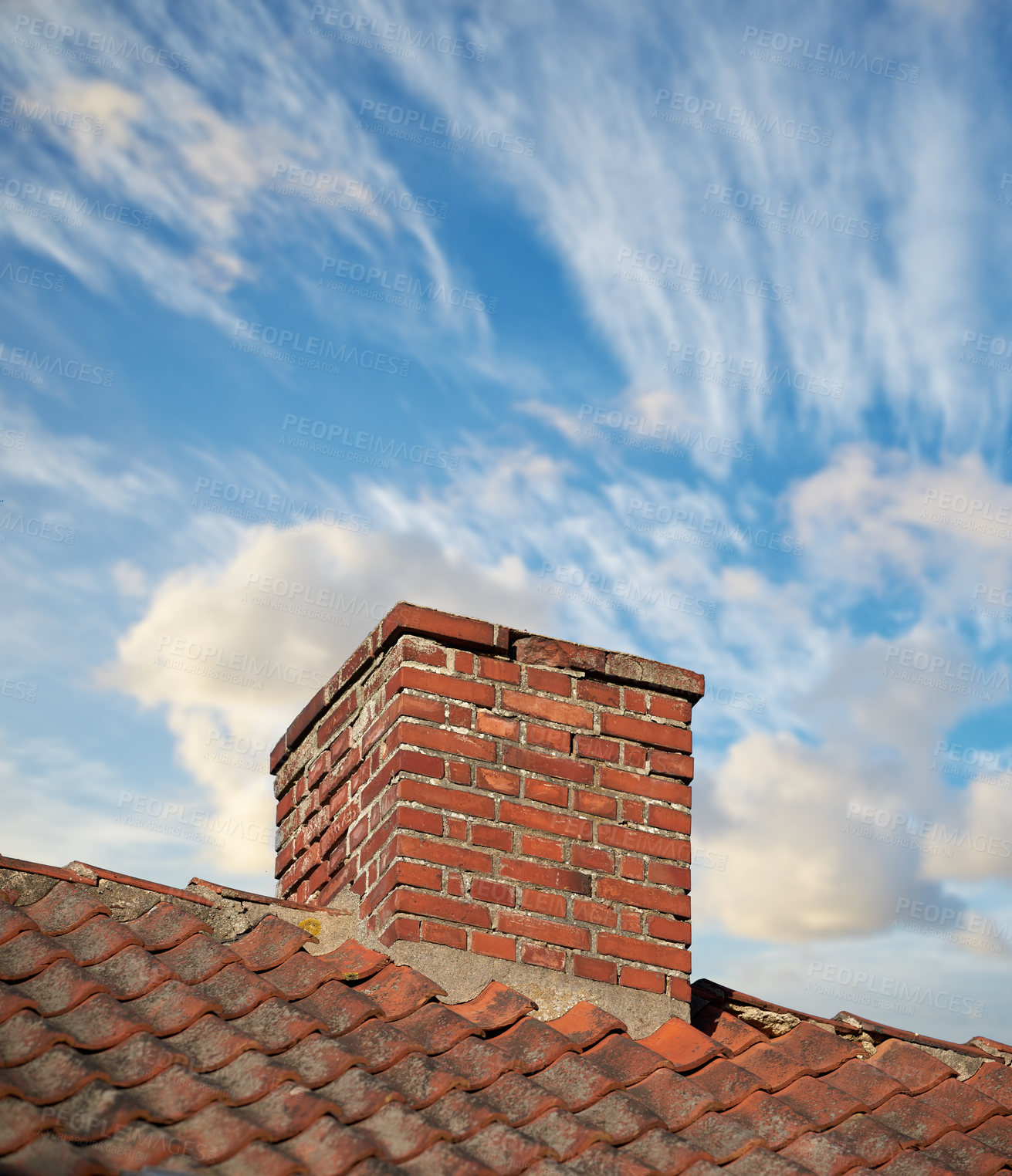 Buy stock photo A brick chimney on the roof in the blue cloudy sky background. A closeup of the chimney on the rooftop. An orange bricked roof with chimney against the blue sky with copy space on a sunny day.