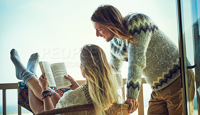 Buy stock photo Shot of a young couple reading a book together while relaxing on the balcony