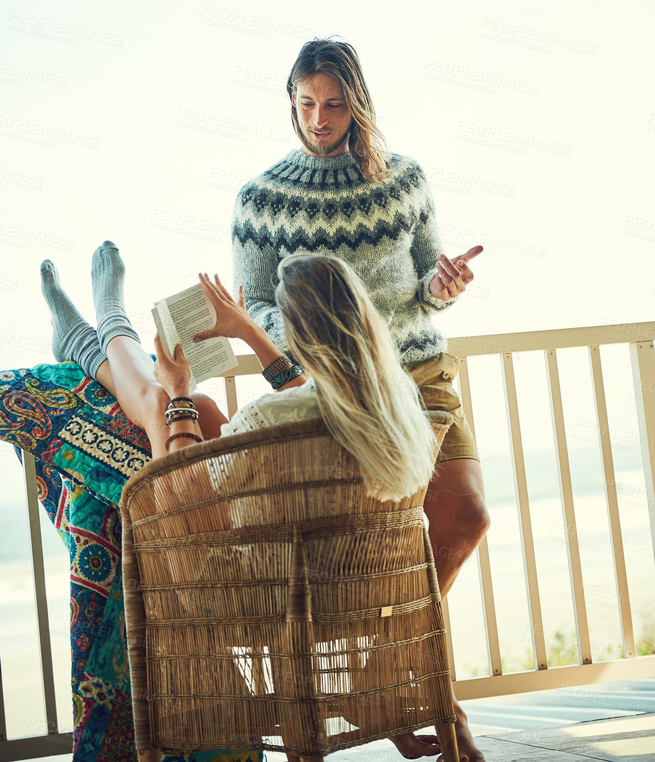 Buy stock photo Shot of a young man chatting with his girlfriend while she reads a book out on the balcony