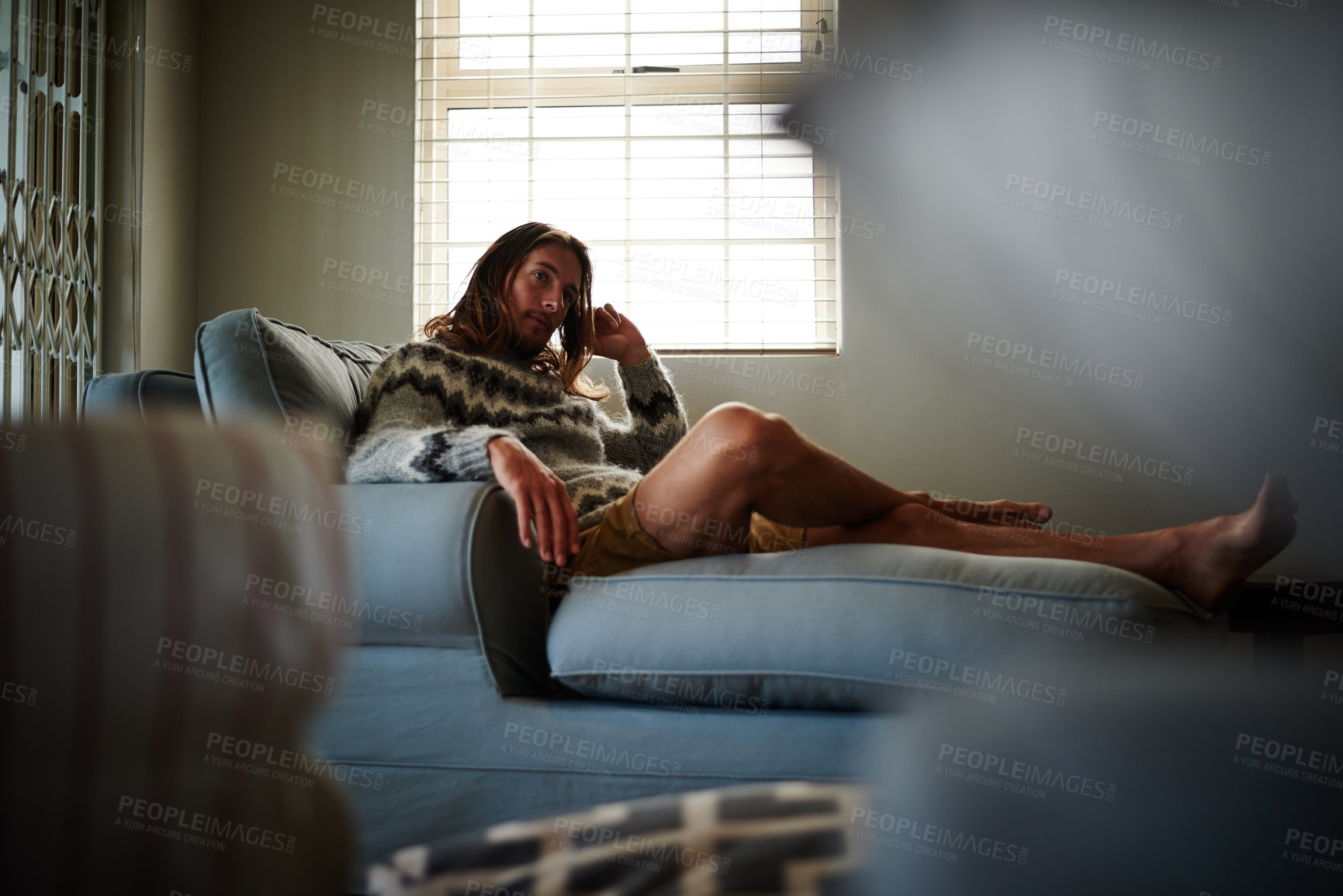 Buy stock photo Full length shot of a young man sitting on his sofa at home