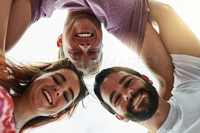 Buy stock photo Low angle shot of a group of young friends looking down and smiling at the camera while standing outside