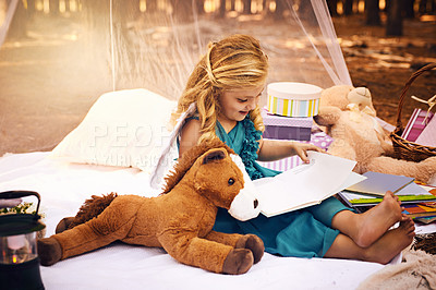 Buy stock photo Shot of a happy little girl reading a storybook while sitting on a blanket outside in the woods