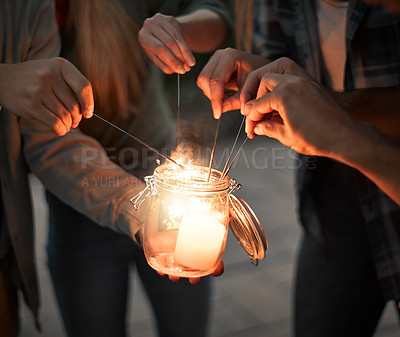Buy stock photo Shot of a group unrecognizable people's hands lighting up sparklers together outside at night