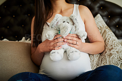 Buy stock photo Shot of an unidentifiable pregnant woman holding a stuffed toy while sitting on her bed at home