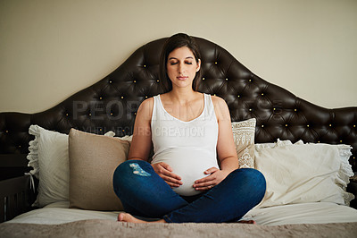 Buy stock photo Shot of a pregnant woman meditating on her bed while cradling her belly