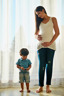 Buy stock photo Shot of a pregnant woman looking at her little boy while he plays with a smartphone