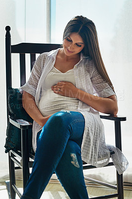 Buy stock photo Shot of a happy pregnant woman cradling her belly while relaxing in a chair at home
