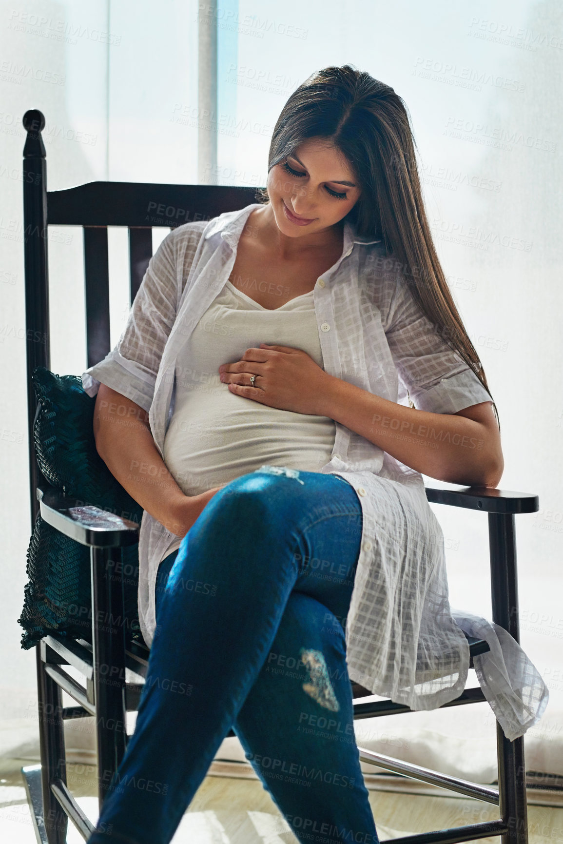 Buy stock photo Shot of a happy pregnant woman cradling her belly while relaxing in a chair at home