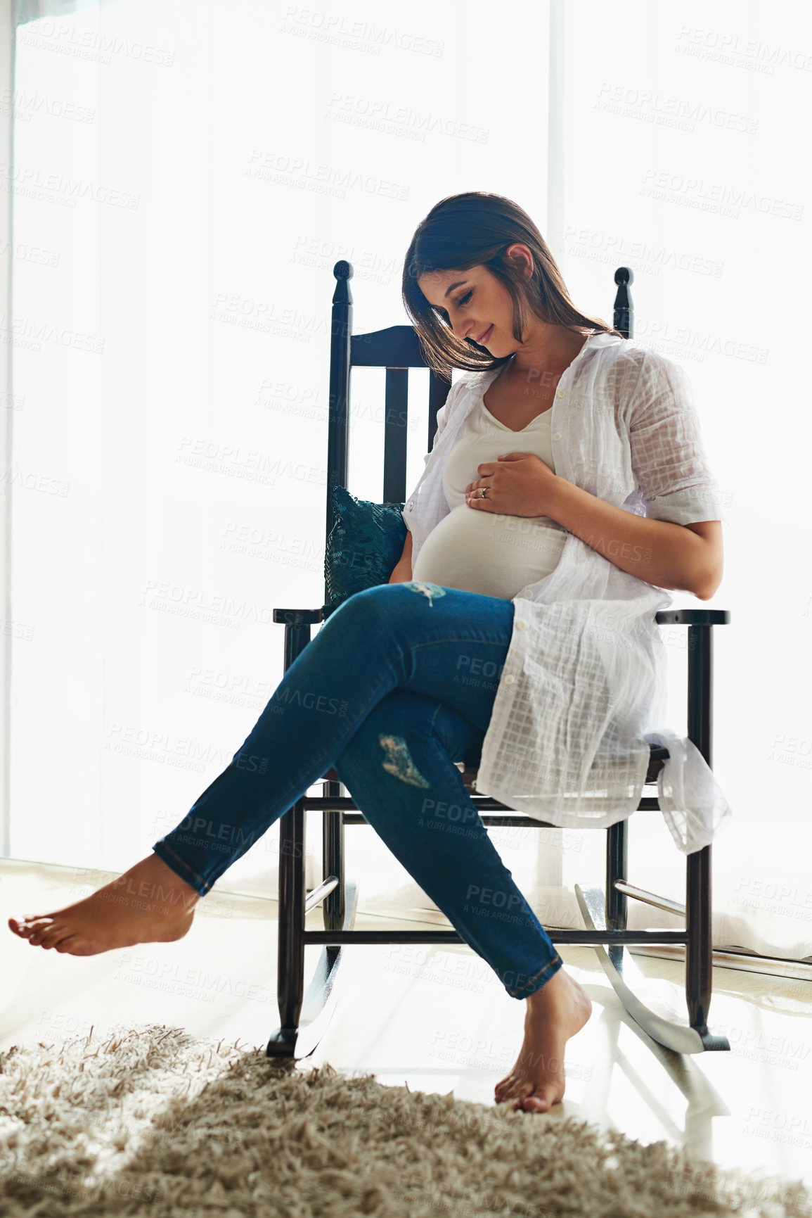 Buy stock photo Shot of a happy pregnant woman cradling her belly while relaxing in a chair at home