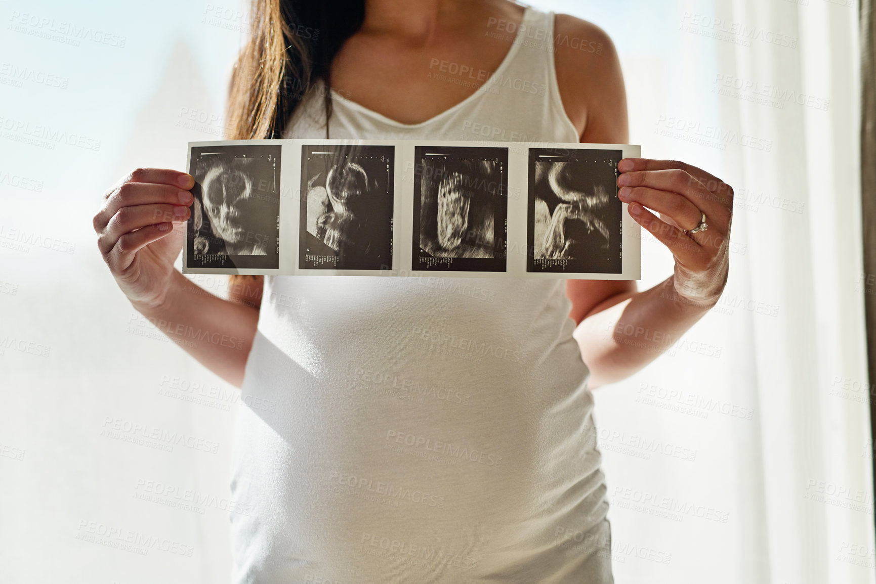 Buy stock photo Shot of an unidentifiable pregnant woman holding up a series of ultrasound pictures in front of a window at home