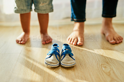 Buy stock photo Shot of an unidentifiable mother and her little boy's feet standing behind a pair of baby shoes at home