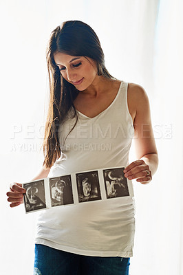 Buy stock photo Shot of a happy pregnant woman holding up a series of ultrasound pictures in front of a window at home