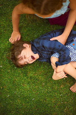 Buy stock photo High angle shot of a young girl tickling her brother while playing outside on the lawn