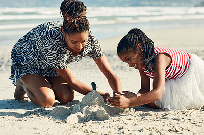 Buy stock photo Shot of a mother and her little daughter building a sandcastle together at the beach