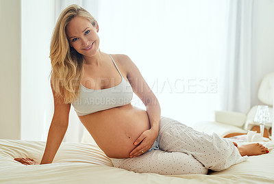 Buy stock photo Shot of a pregnant woman touching her belly while sitting on her bed