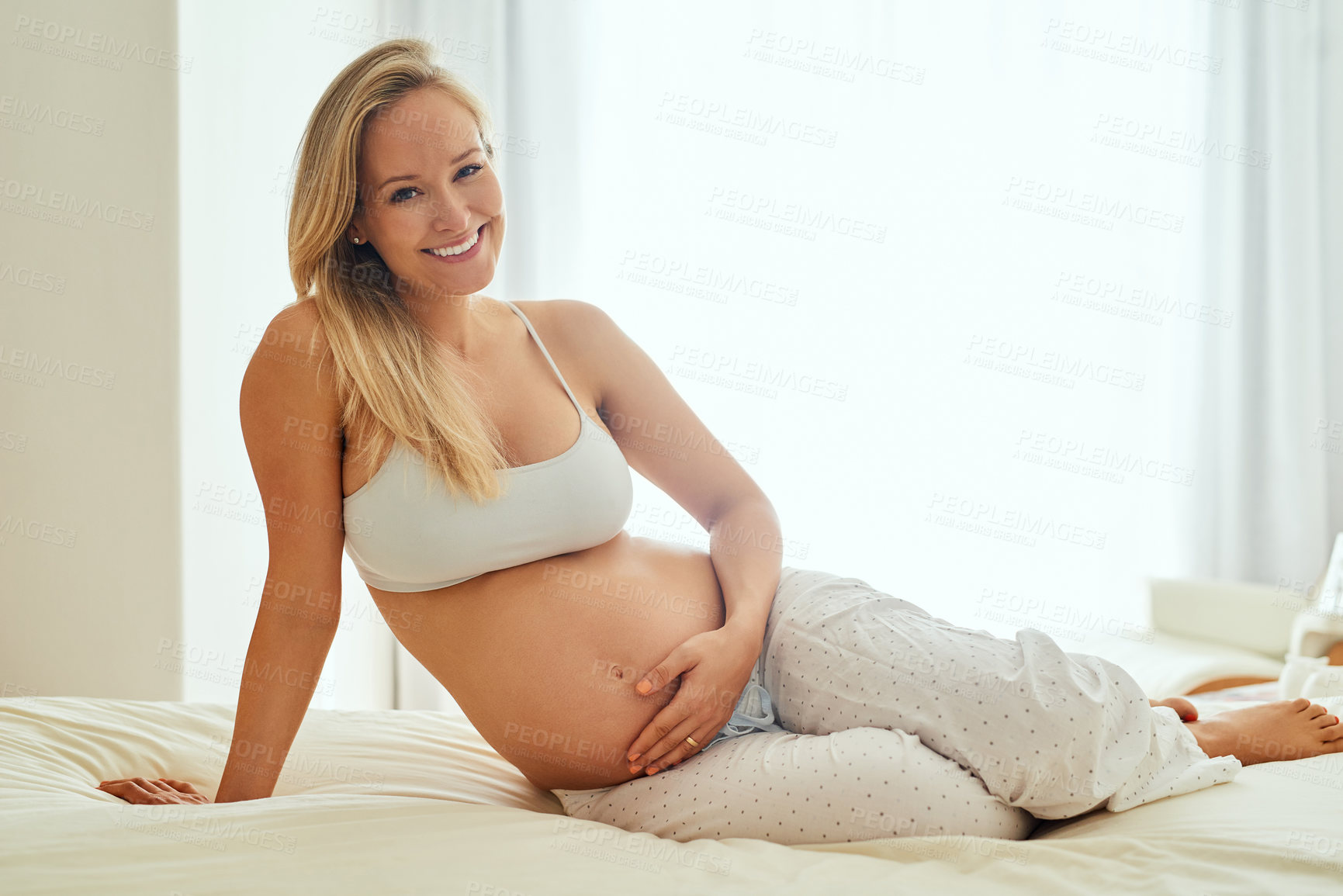 Buy stock photo Shot of a pregnant woman touching her belly while sitting on her bed