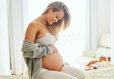 Buy stock photo Shot of a pregnant woman touching her belly while sitting on her bed
