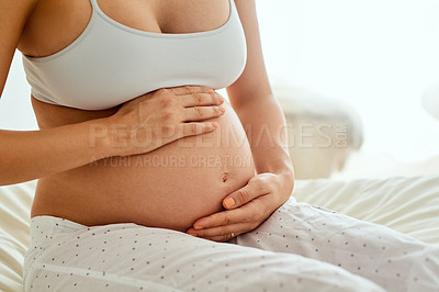 Buy stock photo Cropped shot of a pregnant woman touching her belly while sitting on her bed