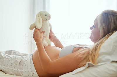 Buy stock photo Shot of a pregnant woman holding a stuffed toy while sitting on her bed