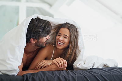 Buy stock photo Shot of a happy young couple laying under a duvet together in bed