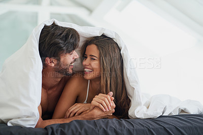 Buy stock photo Shot of a happy young couple laying under a duvet together in bed