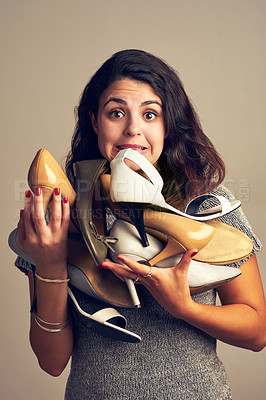 Buy stock photo Studio shot of a joyful young woman holding a lot of shoes against a brown background