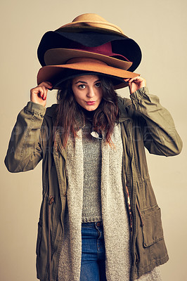 Buy stock photo Studio shot of a young woman wearing a pile of hats against a brown background