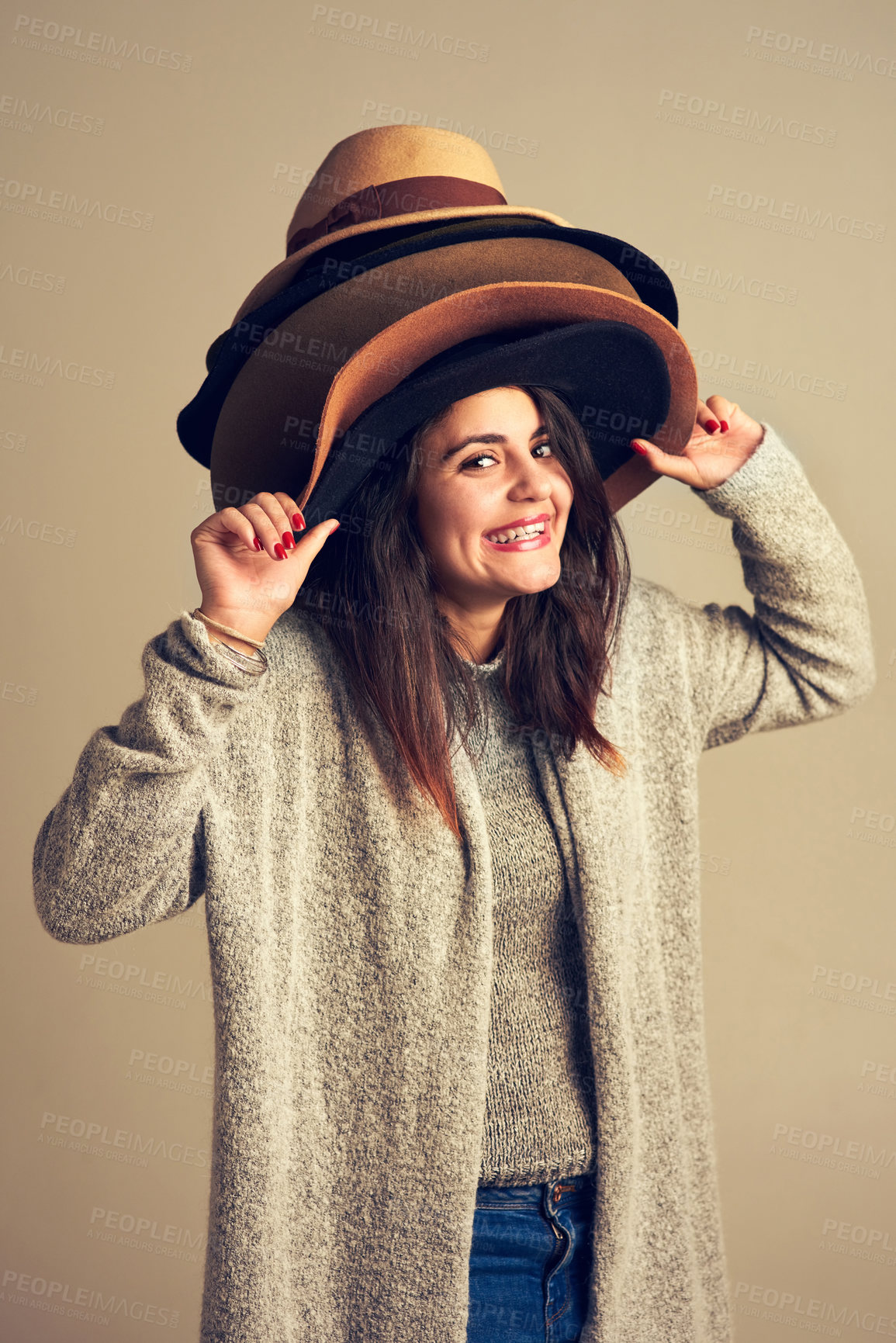 Buy stock photo Woman, studio and fashion portrait with hats, accessory and choices for outfit on brown background. Happy, style pile and consumerism for shopper with option, trendy obsession and retail selection